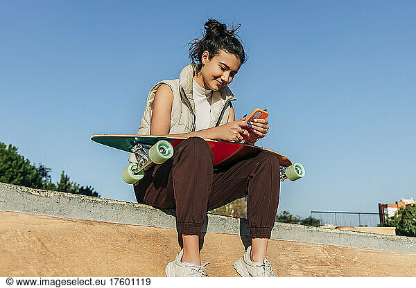Woman with skateboard using mobile phone in sports ramp at park