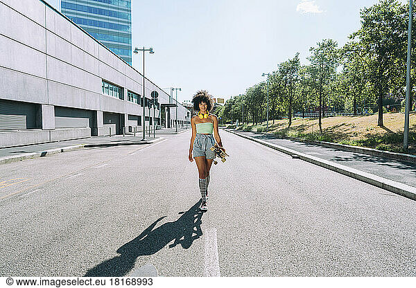 Woman with skateboard walking on road