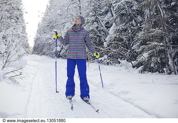 Woman with ski equipment looking up while standing on snow covered field
