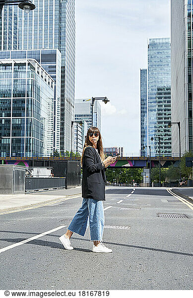 Woman with smart phone crossing road on sunny day