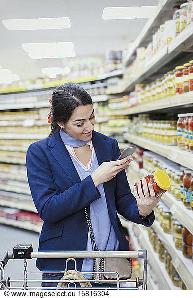 Woman with smart phone scanning label on jar in supermarket