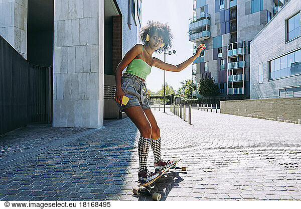 Woman with smart phone skating on longboard outside building