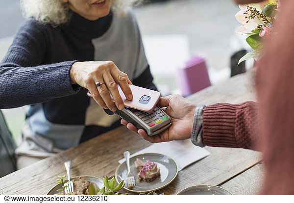 Woman with smart phone using contactless payment at cafe
