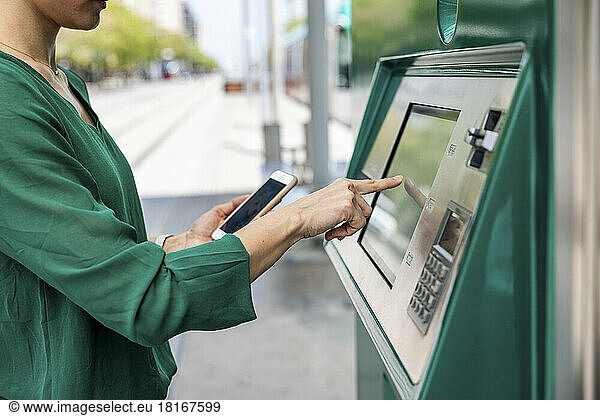 Woman with smart phone using ticket machine