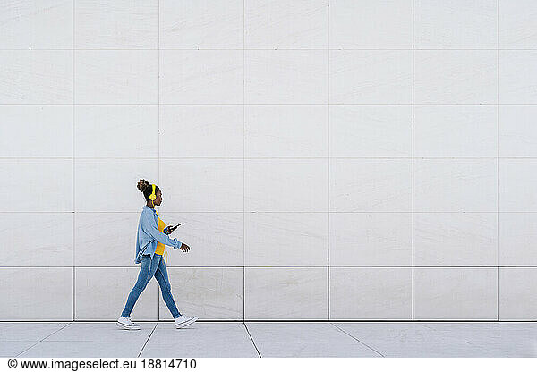 Woman with smart phone walking in front of wall