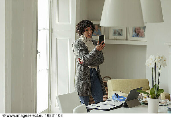 Woman with smart phone working from home at window