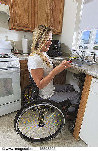 Woman with spinal cord injury in her accessible kitchen using a mobile phone