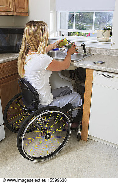Woman with spinal cord injury in her accessible kitchen washing dishes