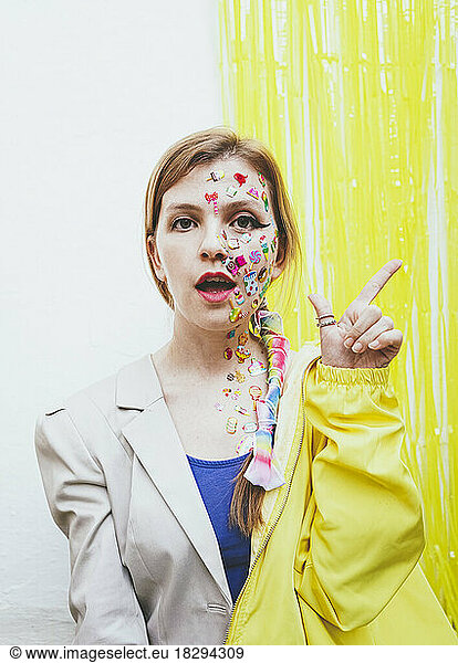 Woman with stickers on face gesturing in front of two tone wall