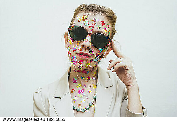 Woman with stickers on face wearing sunglasses in front of white background