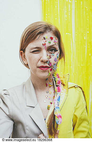 Woman with stickers on face winking in front of two tone wall