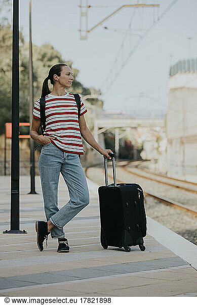 Woman with suitcase waiting for train on railway platform