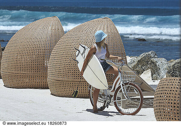 Woman with surfboard riding bicycle on the beach
