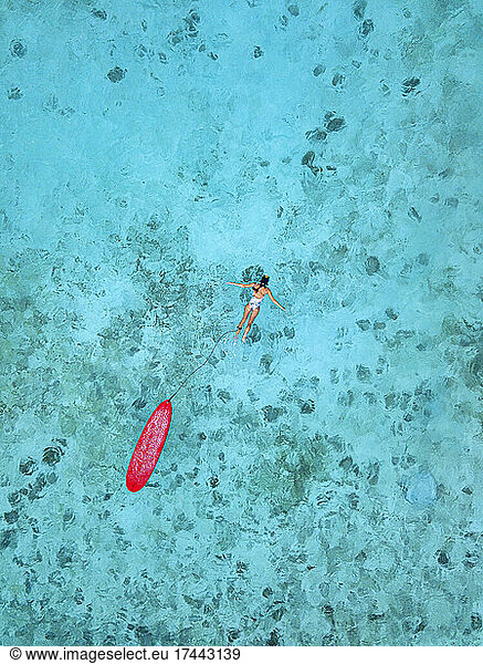 Woman with surfboard swimming in blue ocean at Huraa island  Maldives