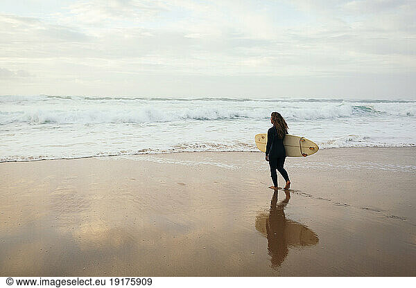 Woman with surfboard walking towards sea at beach