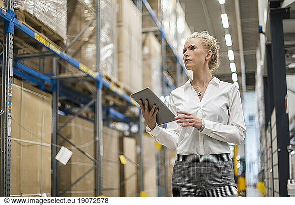 Woman with tablet in factory storehouse looking at shelf