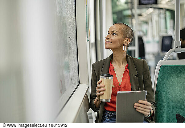Woman with tablet PC and drink container sitting in tram