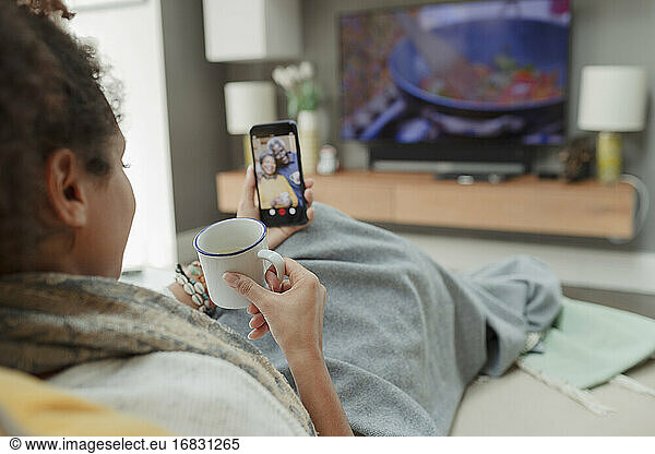 Woman with tea video chatting with parents on smart phone screen