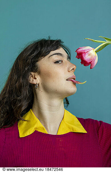 Woman with tulip petal in mouth against green background