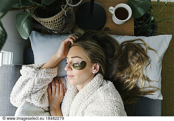 Woman with under eyes patch sleeping on bed at home