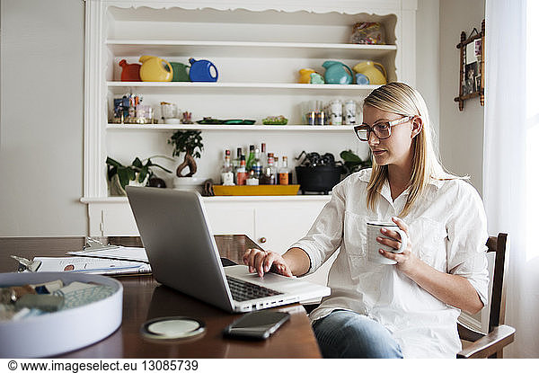 Woman with using laptop while holding mug at home
