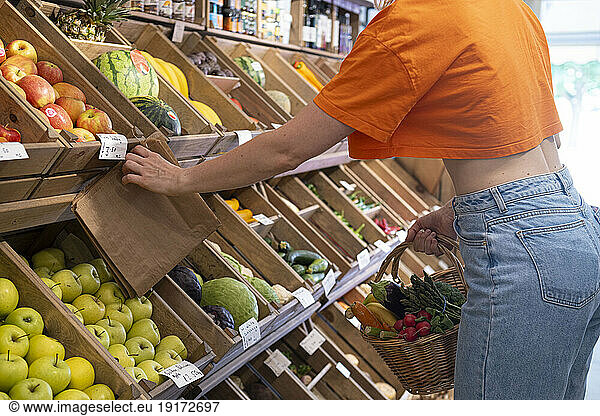 Woman with vegetable basket taking paper bag from rack in store