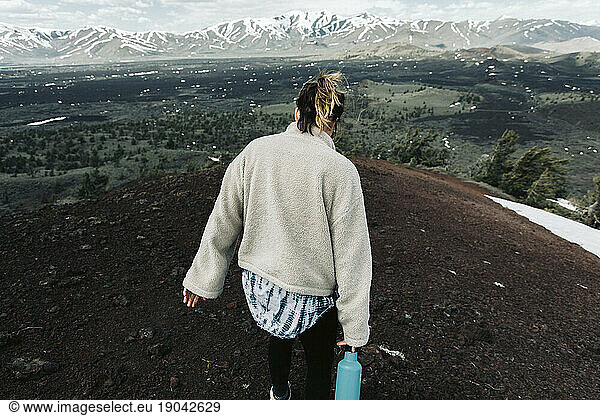 woman with water bottle walks along a ridge at the top of a hike