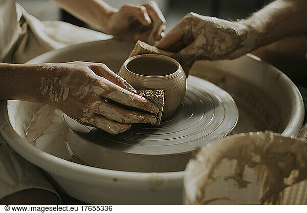 Woman with young man shaping bowl on potter's wheel in workshop