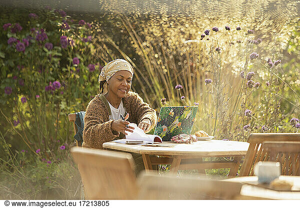 Woman working at laptop at idyllic garden cafe table