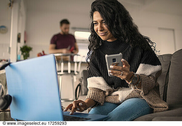 Woman working from home with laptop and smart phone on sofa