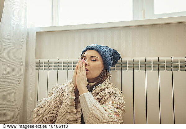Woman wrapped in blanket rubbing hands leaning on radiator