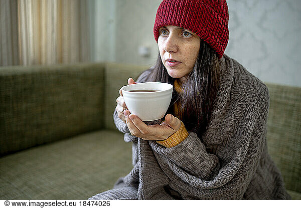 Woman wrapped in blanket sitting with cup of tea at home