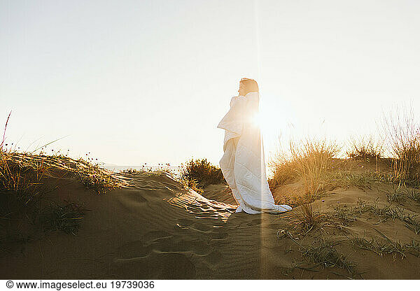 Woman wrapped in blanket standing at beach on sunny day