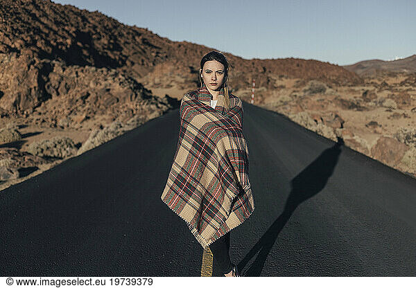 Woman wrapped in blanket standing on road near volcanic landscape