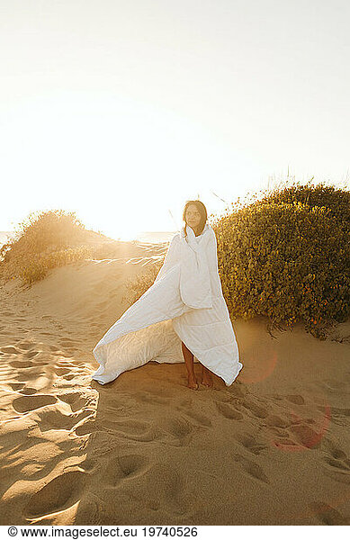 Woman wrapped in blanket standing on sand at beach