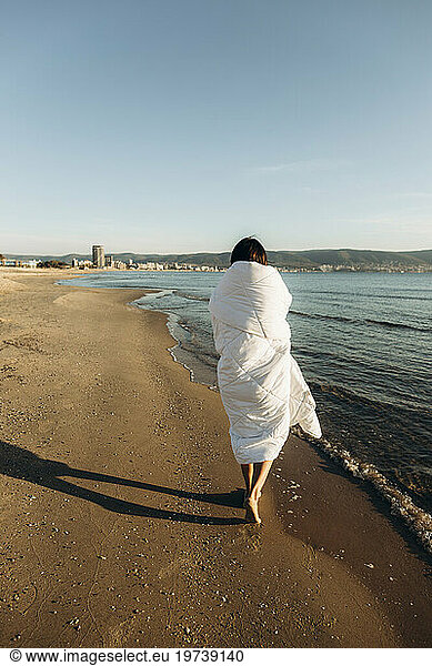 Woman wrapped in blanket walking on sand at beach