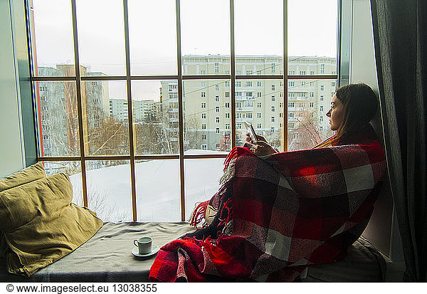 Woman wrapped in blanket while sitting on alcove window seat