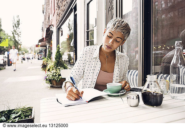 Woman writing in diary at sidewalk cafe