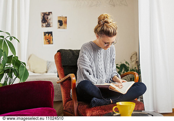 Woman writing on book while sitting on chair at home