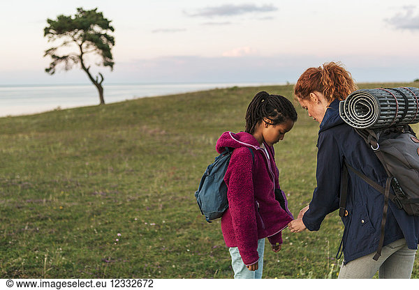 Woman zipping jacket on daughter at field during sunset