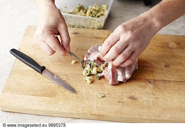 Womans hands stuffing pork steaks on chopping board