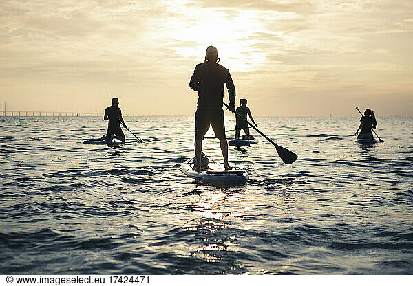 Women and man paddleboarding while spending leisure time in sea