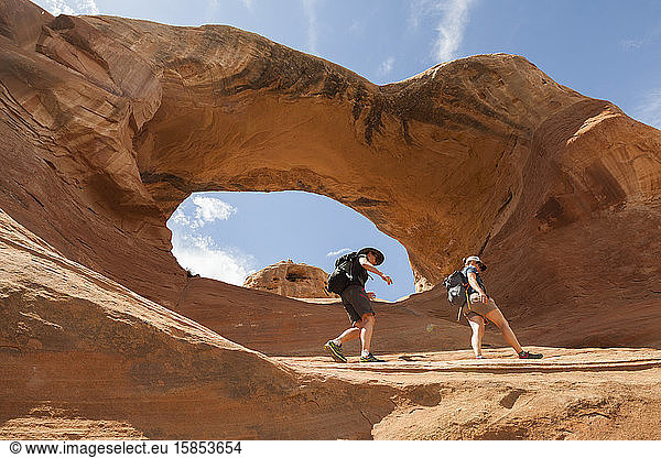 Women hike below sandstone rock arch  McInnis Canyons  Colorado