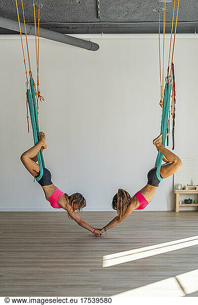 Women holding hands hanging from aerial silk in health club