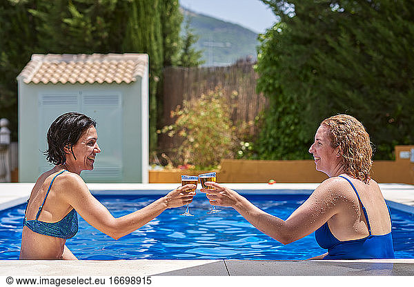 Women in a pool. They toast celebrating that they are on vacation.
