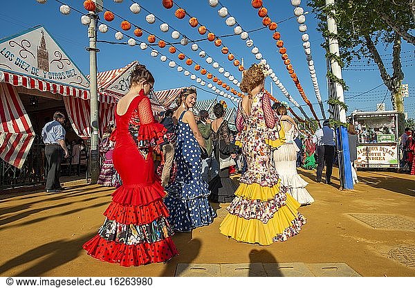 Women in colourful flamenco dresses  in front of marquees  casetas  decorated street  Feria de Abril  Sevilla  Andalusia  Spain  Europe