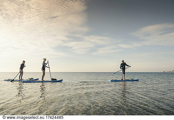 Women learning to paddleboard from male instructor during sunset