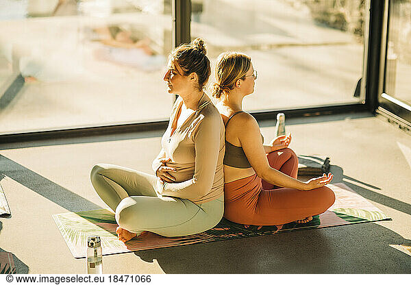 Women practicing breathing exercise sitting back to back during yoga class