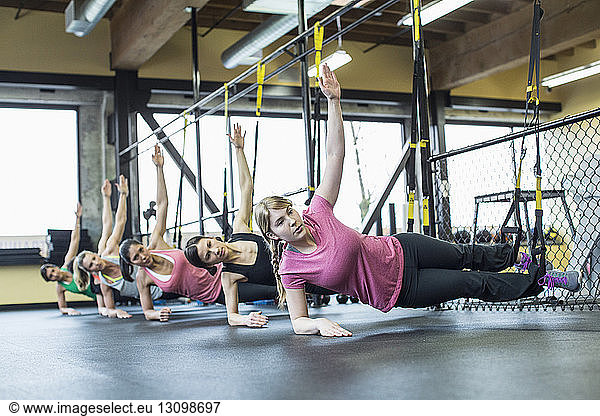 Women practicing side plank pose while balancing on resistance bands in gym