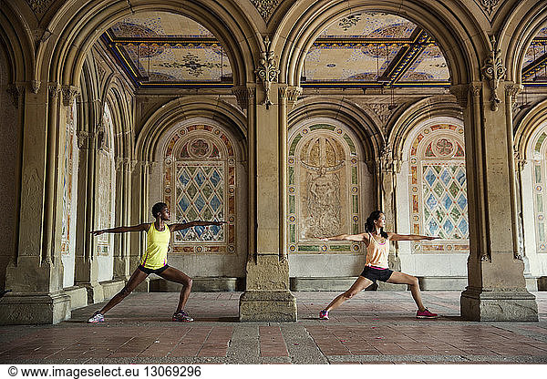 Women practicing warrior 2 position while exercising in historic building